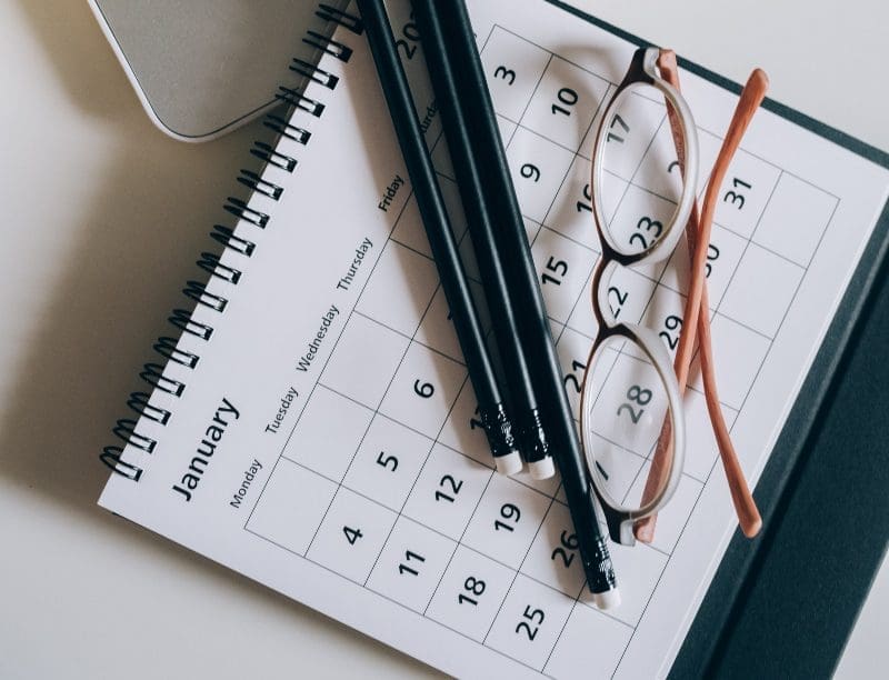A calendar lays on a table with pencils and eye glasses.