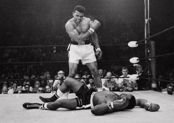 A boxer gloats over his defeated opponent in the ring.