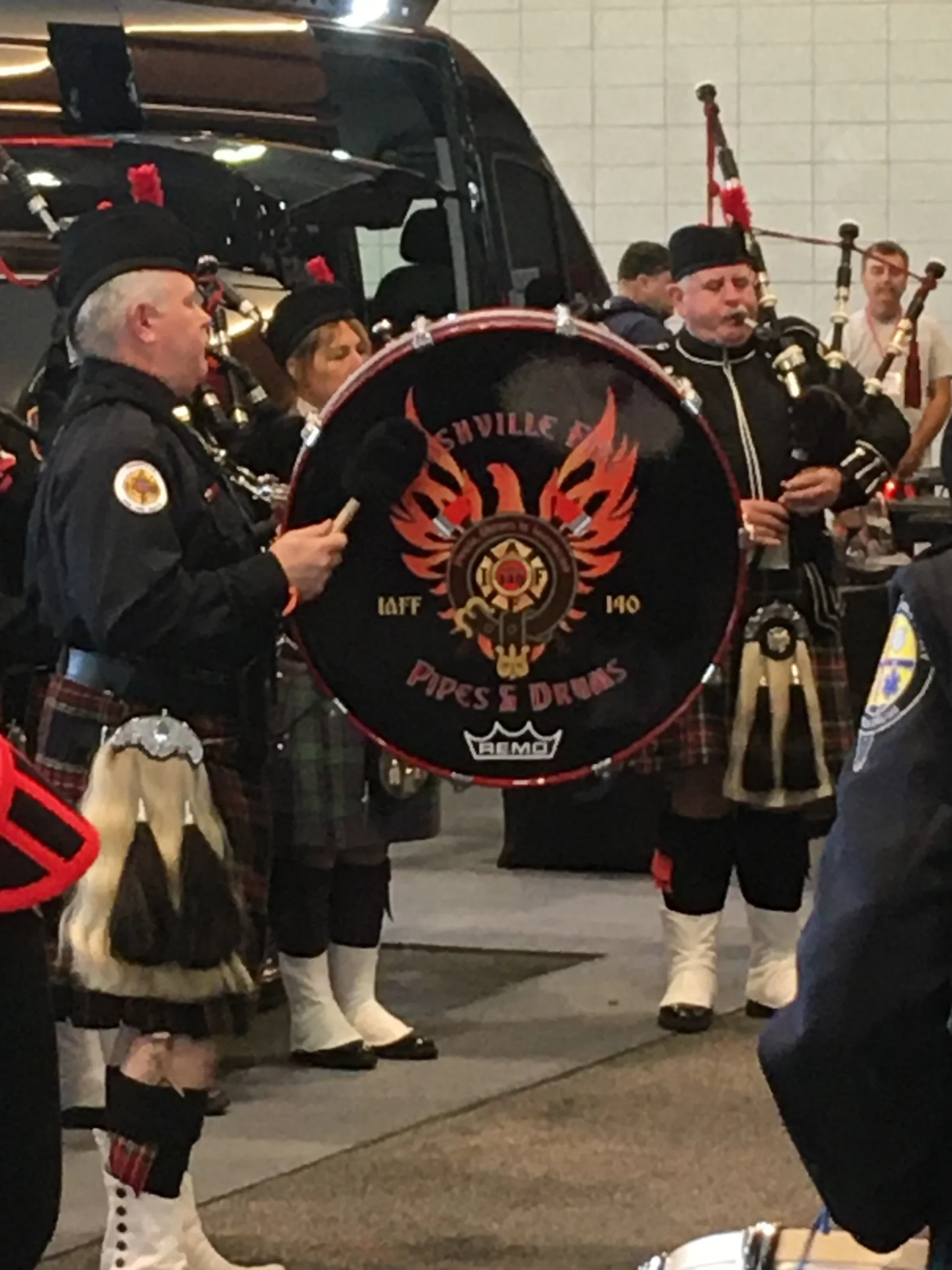 Bagpipers play beside a base drum labeled with a firefighter pipe and drum unit's logo at the 2019 Firehouse Expo.